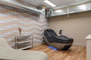 A massage chair with a blue light underneath it sits in a room with a tiled wall behind it.